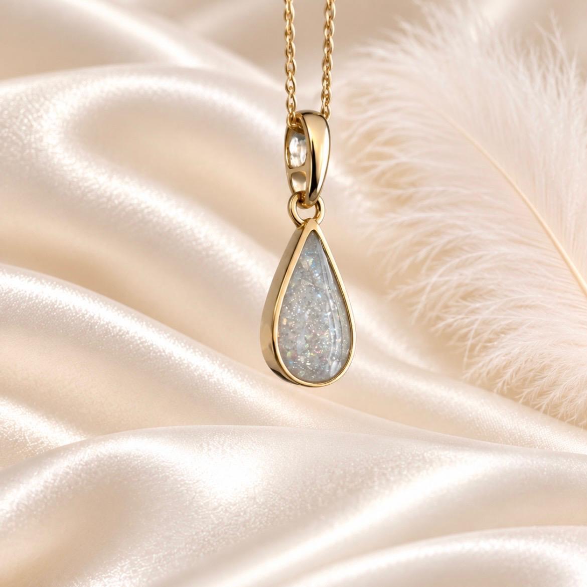 Keepsake Memorial Jewellery gold teardrop pendant necklace with a shimmering grey inlay on a satin background.