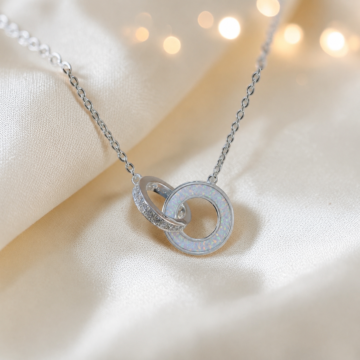 Eternal Embrace Pendant in  sterling silver — two interlocking rings with cubic zirconia. Shown in white snow.Handcrafted memorial jewellery, made in Lancashire Uk -by Keepsake Memorial Jewellery