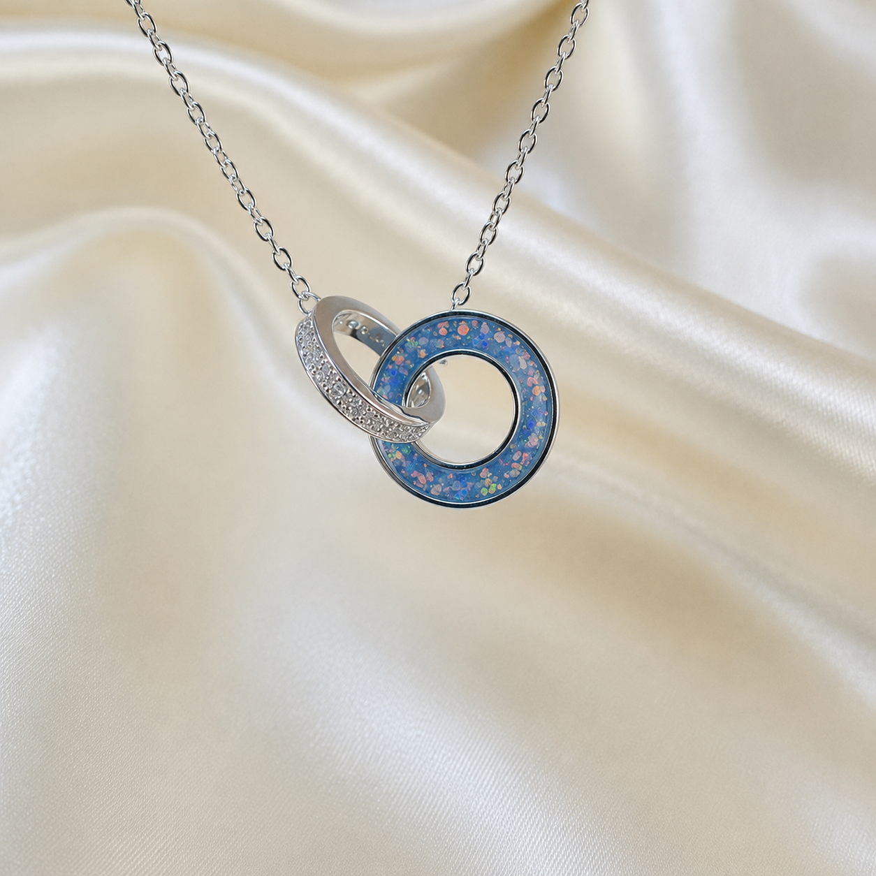 Eternal Embrace Pendant in 925 sterling silver — two interlocking rings with cubic zirconia in baby blue. Handcrafted memorial jewellery, made in Lancashire Uk -by Keepsake Memorial Jewellery