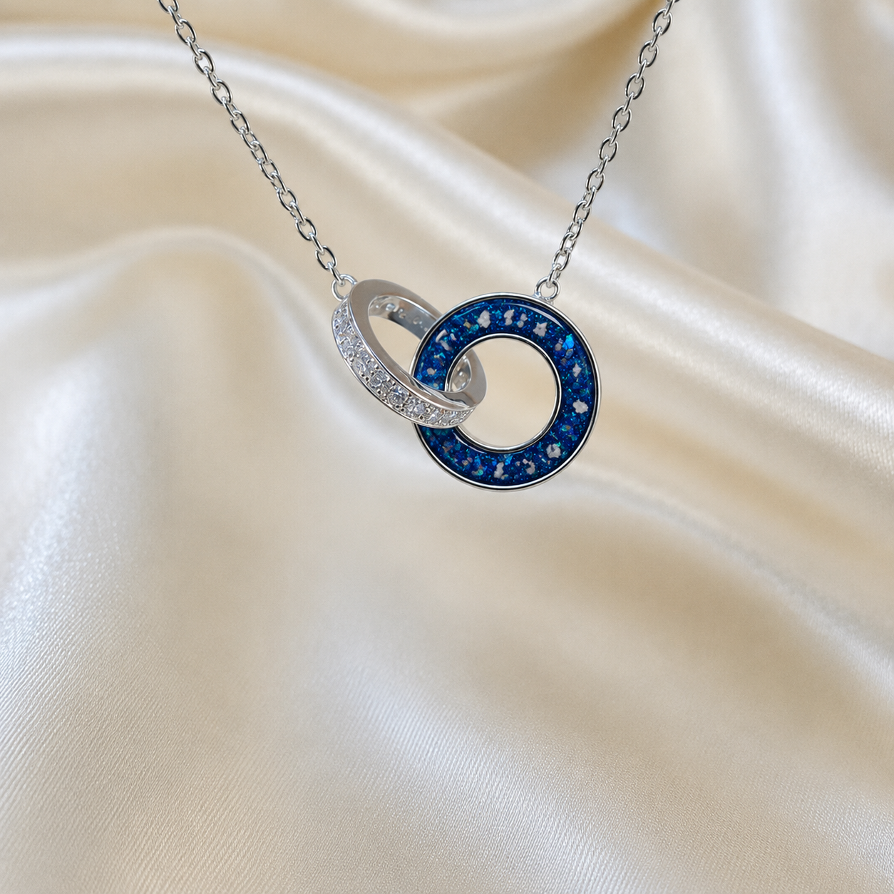 Eternal Embrace Pendant in 925 sterling silver — two interlocking rings with cubic zirconia in sapphire glow. Handcrafted memorial jewellery, made in Lancashire Uk -by Keepsake Memorial Jewellery