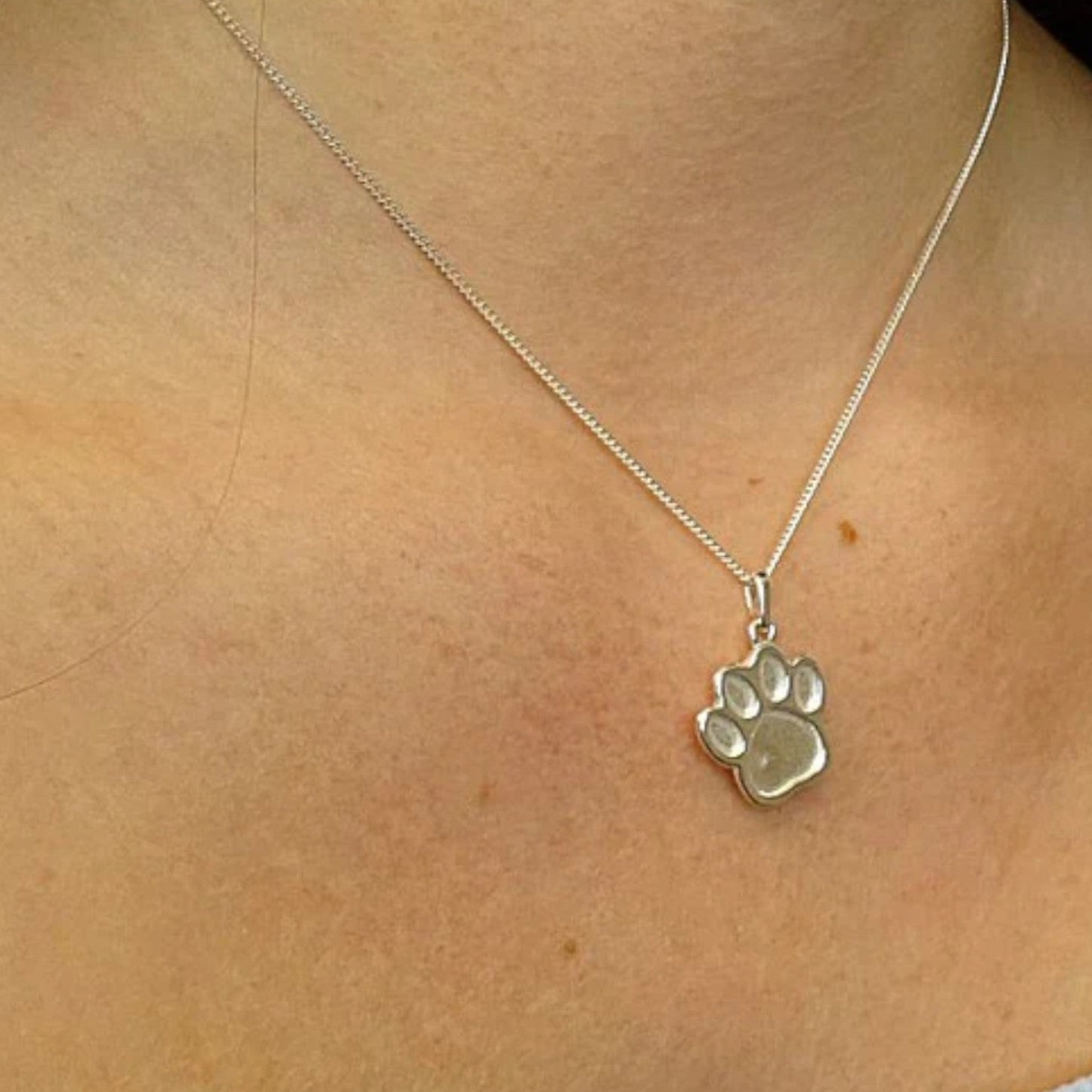Silver paw print necklace on a person's neck