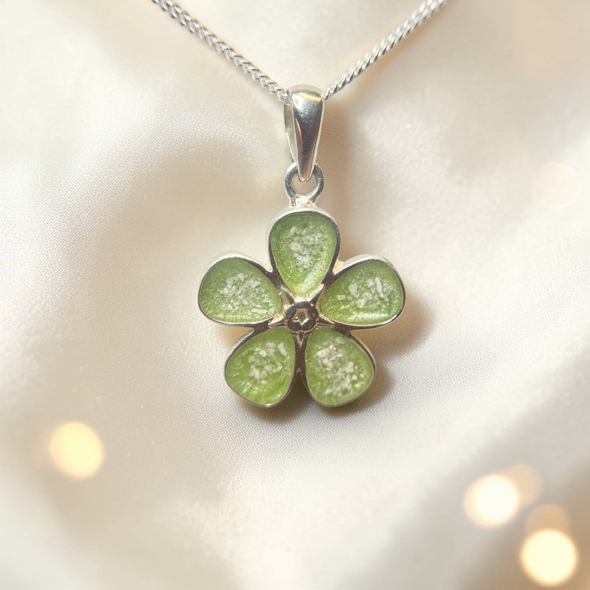 Green flower-shaped pendant on a silver chain against a soft background