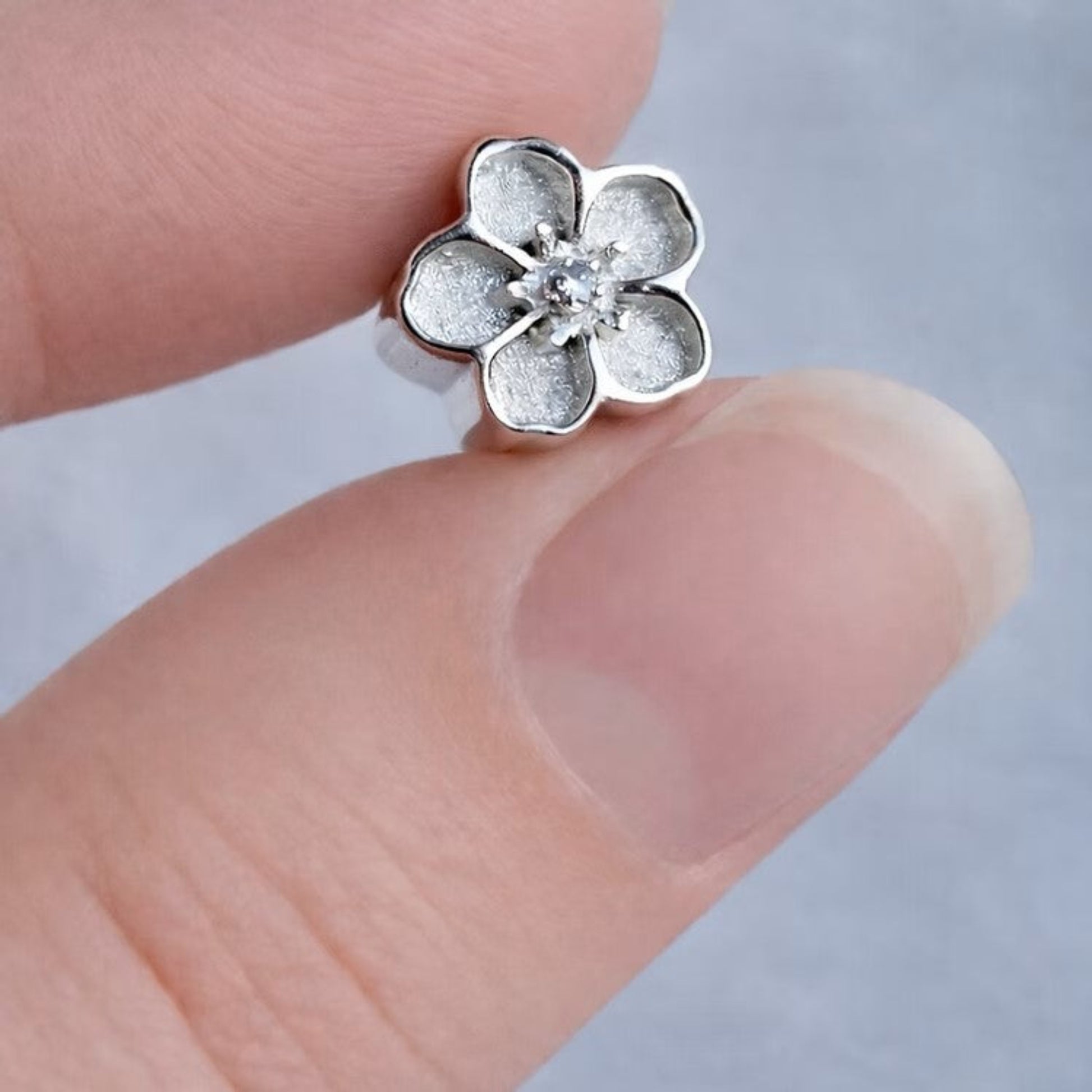 Silver flower-shaped earring held between fingers against a neutral background