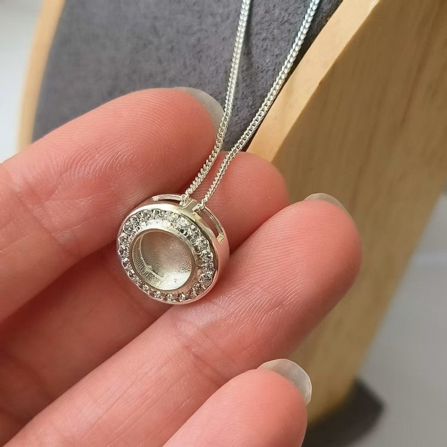 Silver necklace with a round pendant held in a hand against a neutral background