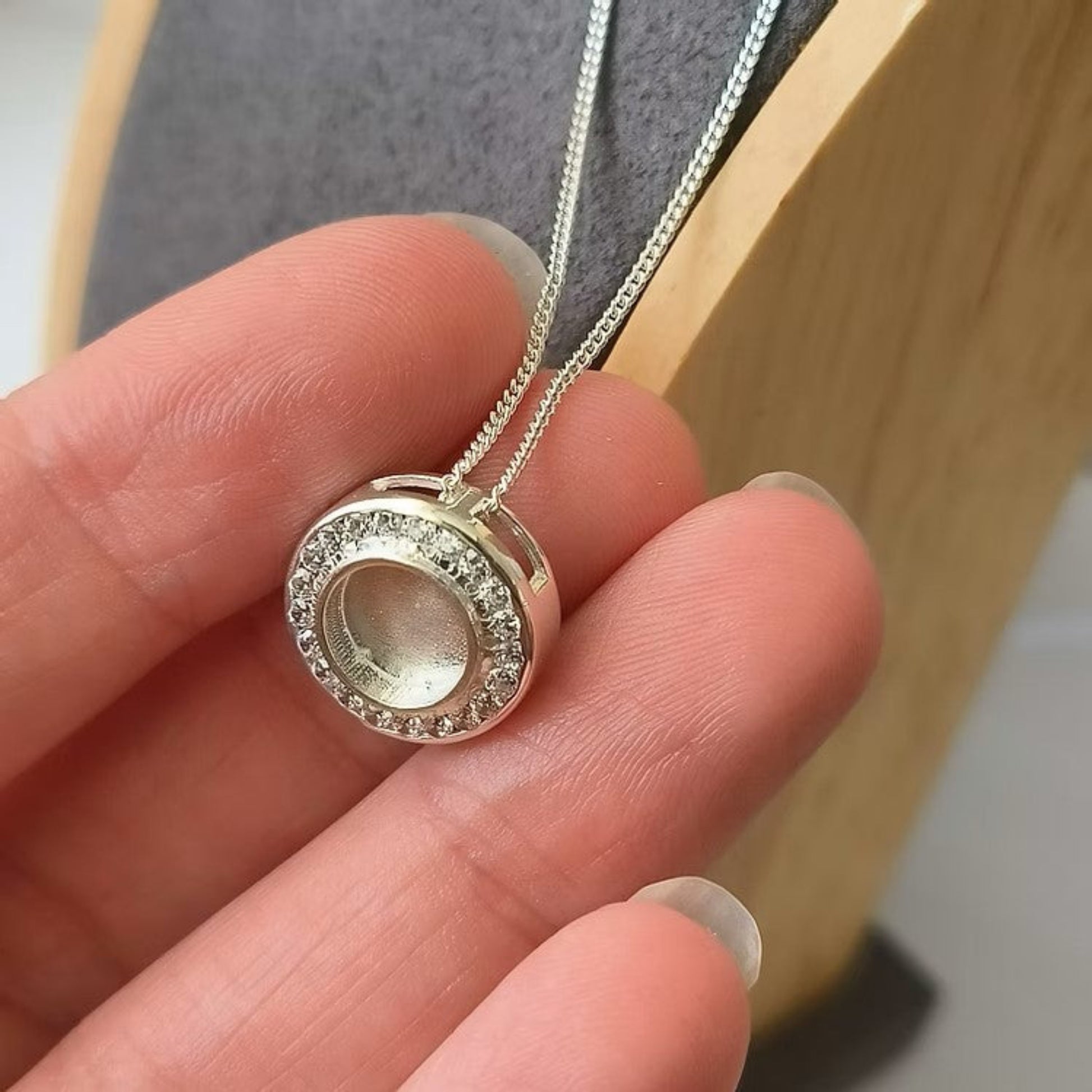 Silver necklace with a round pendant held in a hand against a neutral background